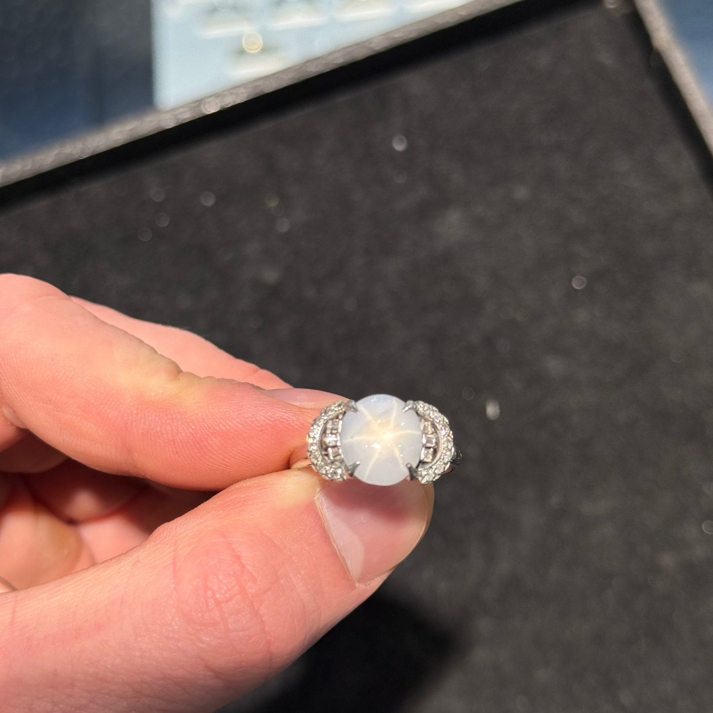A blueish grey star sapphire and diamond ring being held to display the star sapphire star