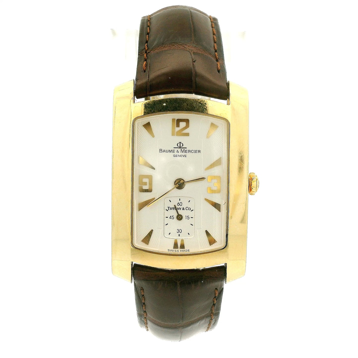 A Vintage Baume & Mercier watch with a 18k gold rectangular case, cream dial with 9, 12 & 3 displayed, the dial is stamped with a tiffany & Co., and dark brown leather strap, shown against a plain white background at Forever Rox Fine Jewelry, Lake Tahoes Best Jewelry Store
