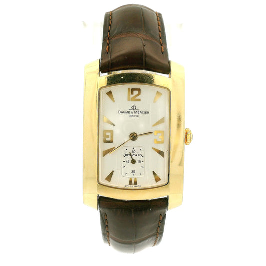 A Vintage Baume & Mercier watch with a 18k gold rectangular case, cream dial with 9, 12 & 3 displayed, the dial is stamped with a tiffany & Co., and dark brown leather strap, shown against a plain white background at Forever Rox Fine Jewelry, Lake Tahoes Best Jewelry Store