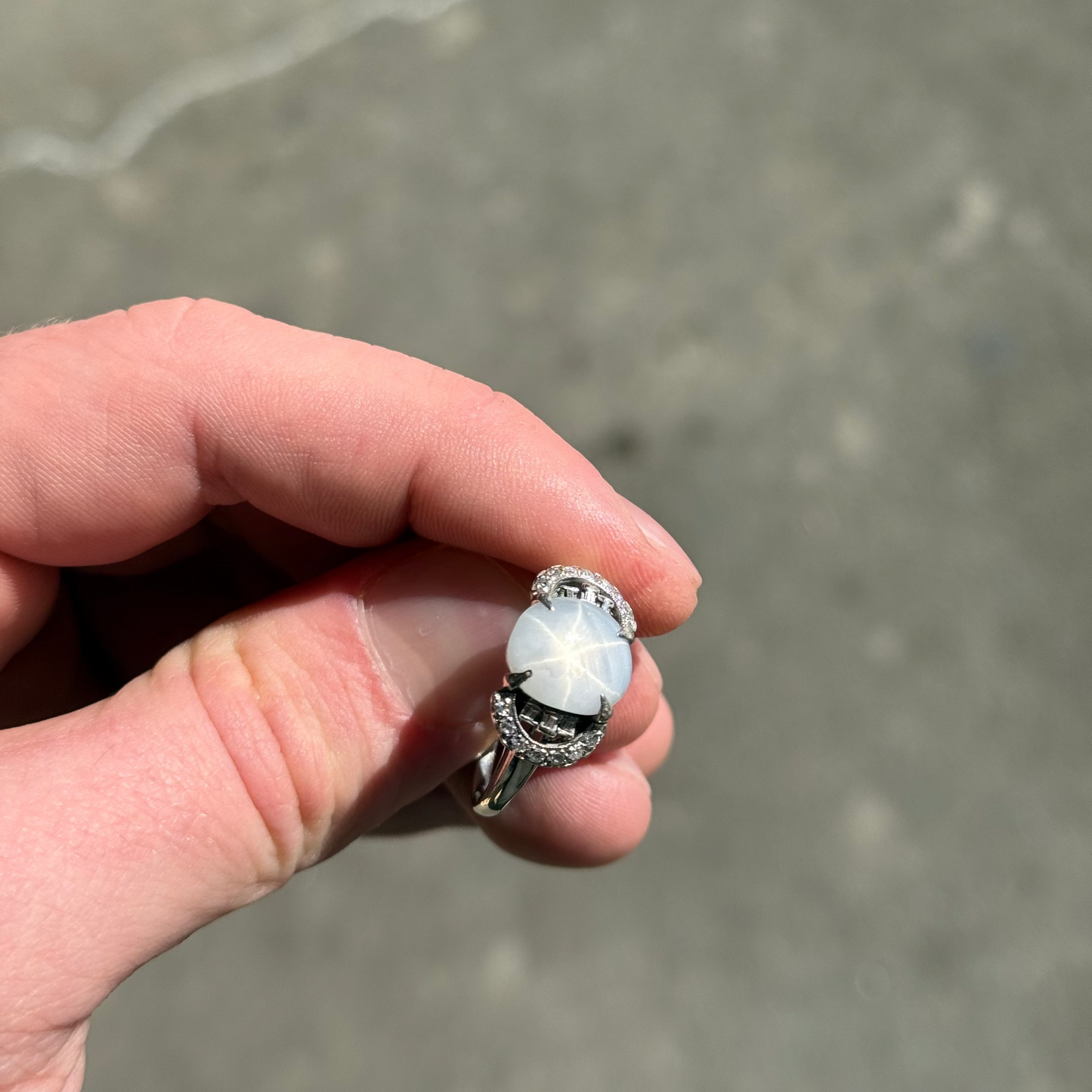 A blueish grey star sapphire and diamond ring being held to display the star sapphire star