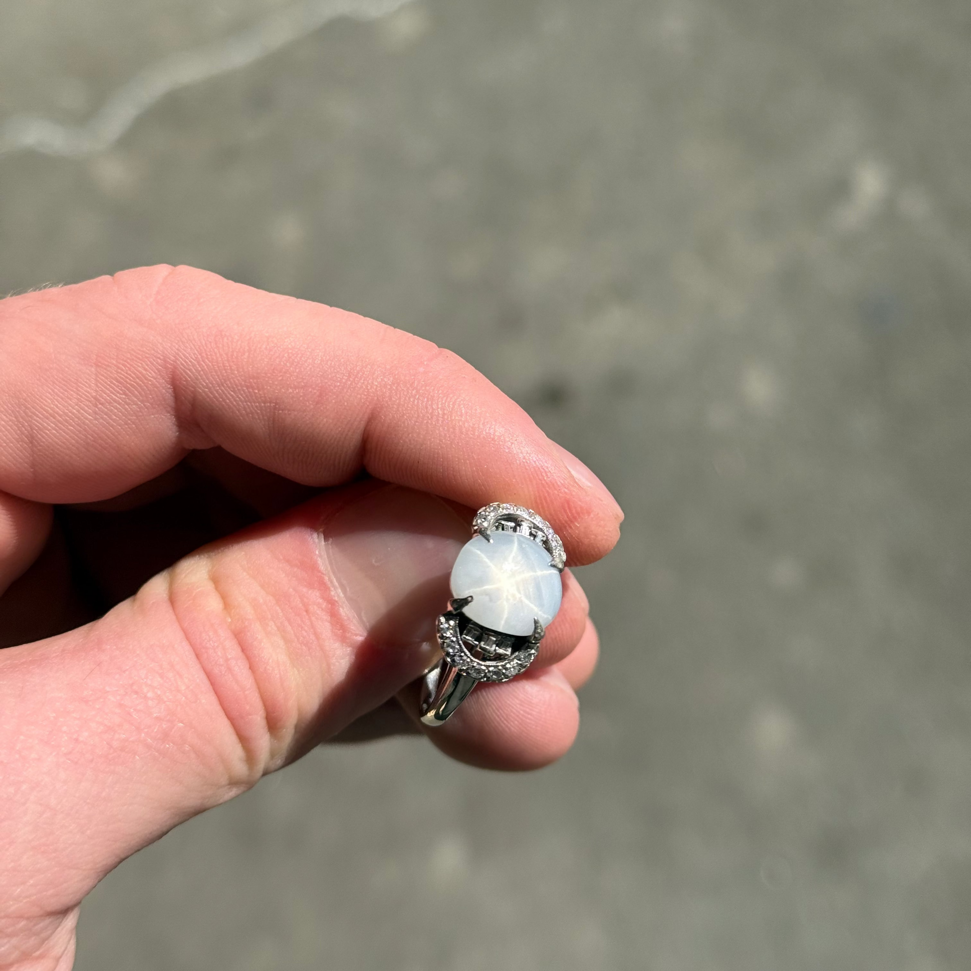 A blueish grey star sapphire and diamond ring being held to display the star sapphire star