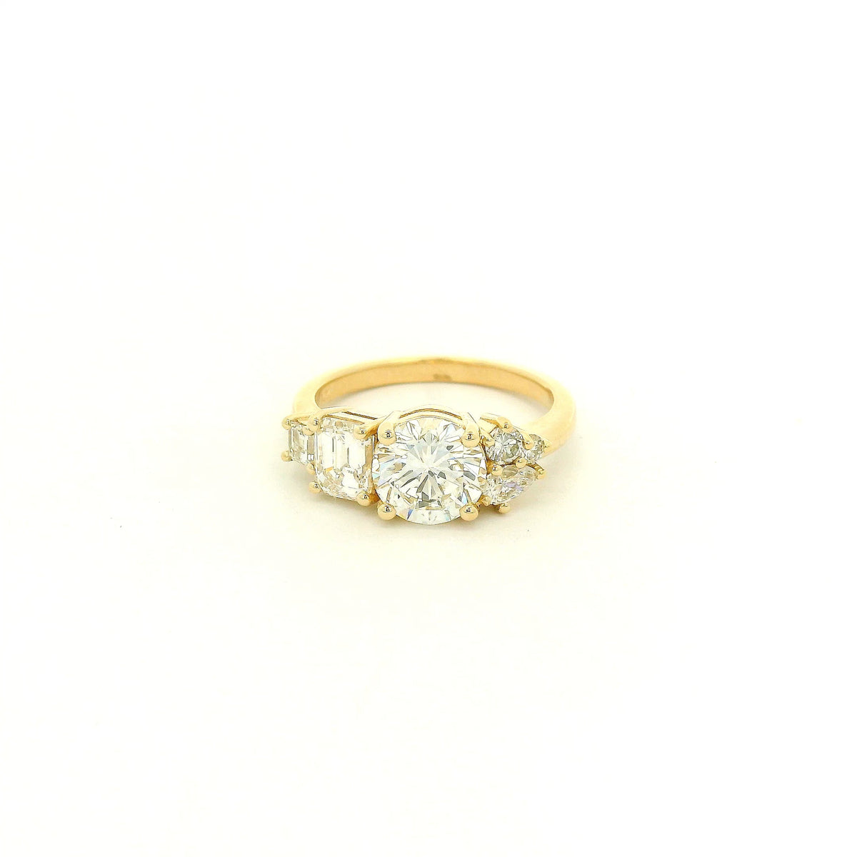 This custom 14k yellow gold engagement ring features a 1.53 ct H-VS2 round brilliant diamond accented by an asymmetrical arrangement of mixed-cut natural diamonds, including a .70 ct F-VVS2 emerald cut, .15 ct G-VS2 pear cut, .17 ct square emerald cut, and two smaller round diamonds. 