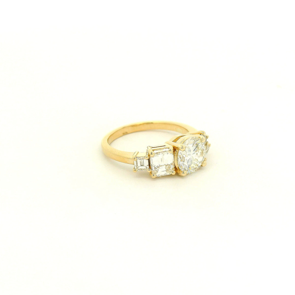 This custom 14k yellow gold engagement ring features a 1.53 ct H-VS2 round brilliant diamond accented by an asymmetrical arrangement of mixed-cut natural diamonds, including a .70 ct F-VVS2 emerald cut, .15 ct G-VS2 pear cut, .17 ct square emerald cut, and two smaller round diamonds. 