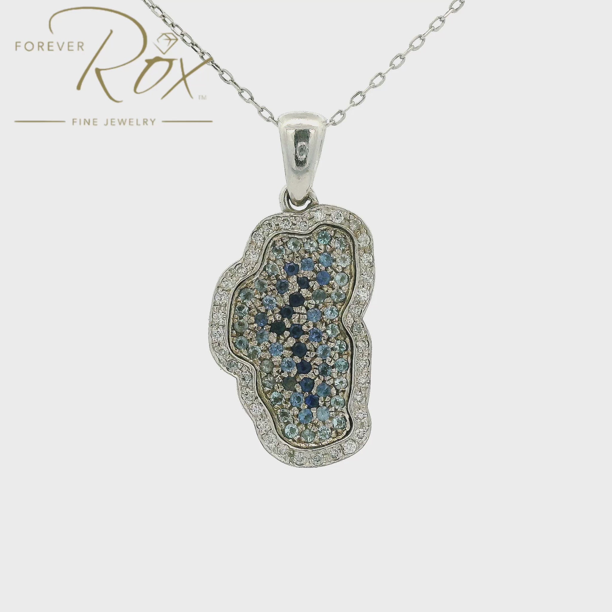 White gold Lake Tahoe outline pendant with different shades of blue sapphires in the center. With Forever Rox Fine Jewelry logo