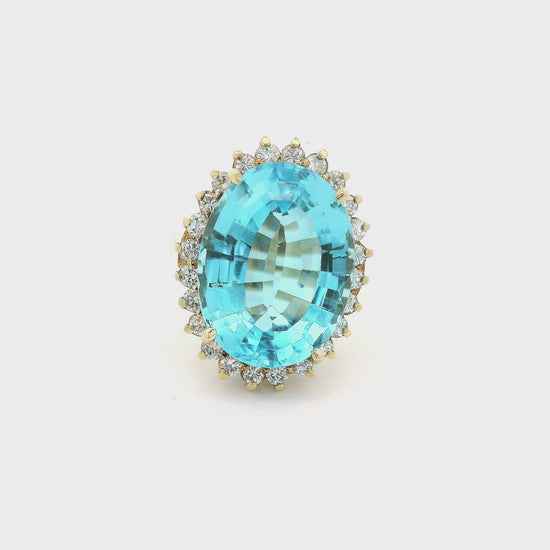A Yellow Gold Coctail Ring with a prong set oval cut light blue Topaz in the center with a halo of diamonds around it at Forever Rox Fine Jewelry, Lake Tahoes Best Jewelry Store