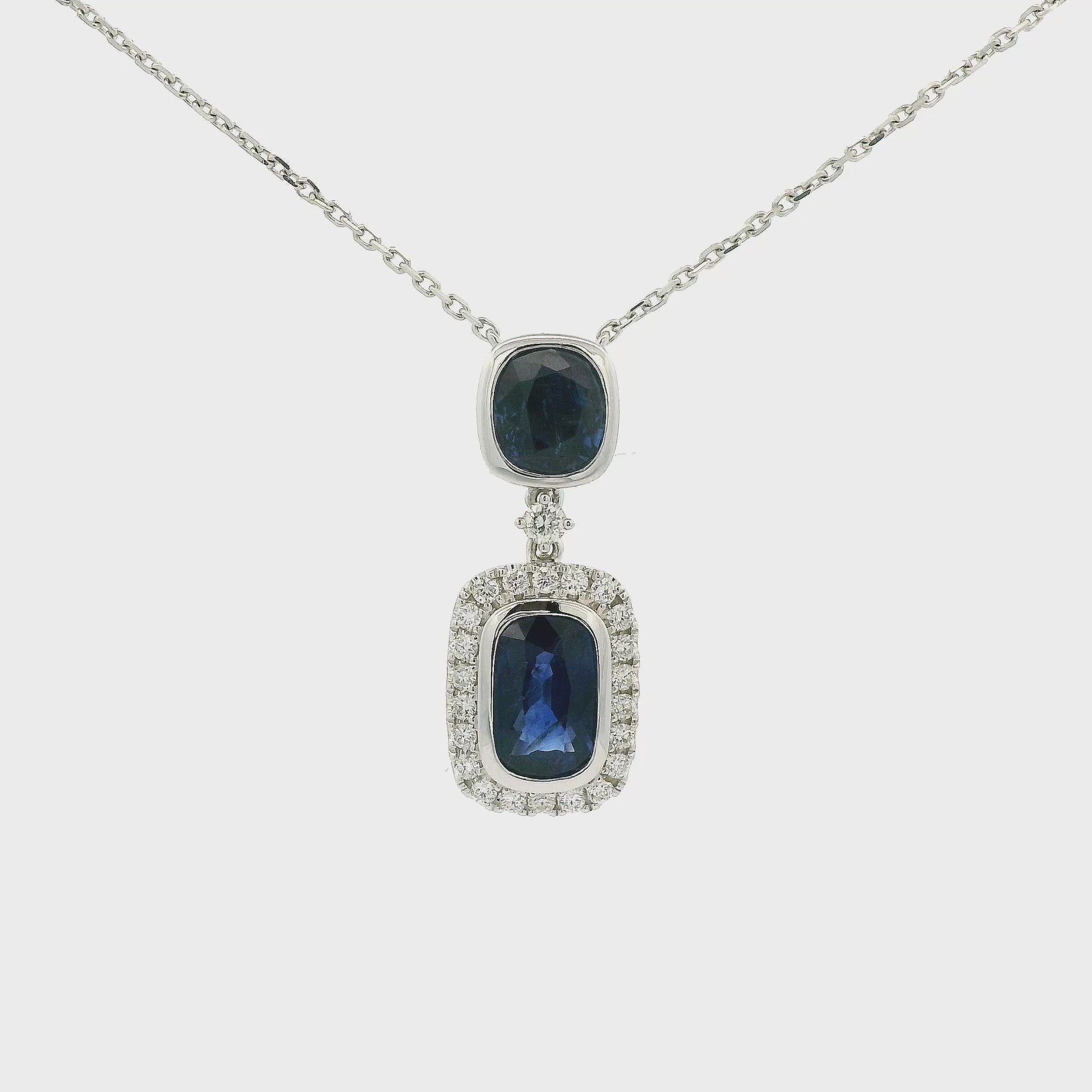 A White Gold Pendant Necklace with two bezel set oval and round cut blue Sapphires in the center with the bottom one having a diamond halo and attached to a diamond by the yard chain at Forever Rox Fine Jewelry, Lake Tahoes Best Jewelry Store