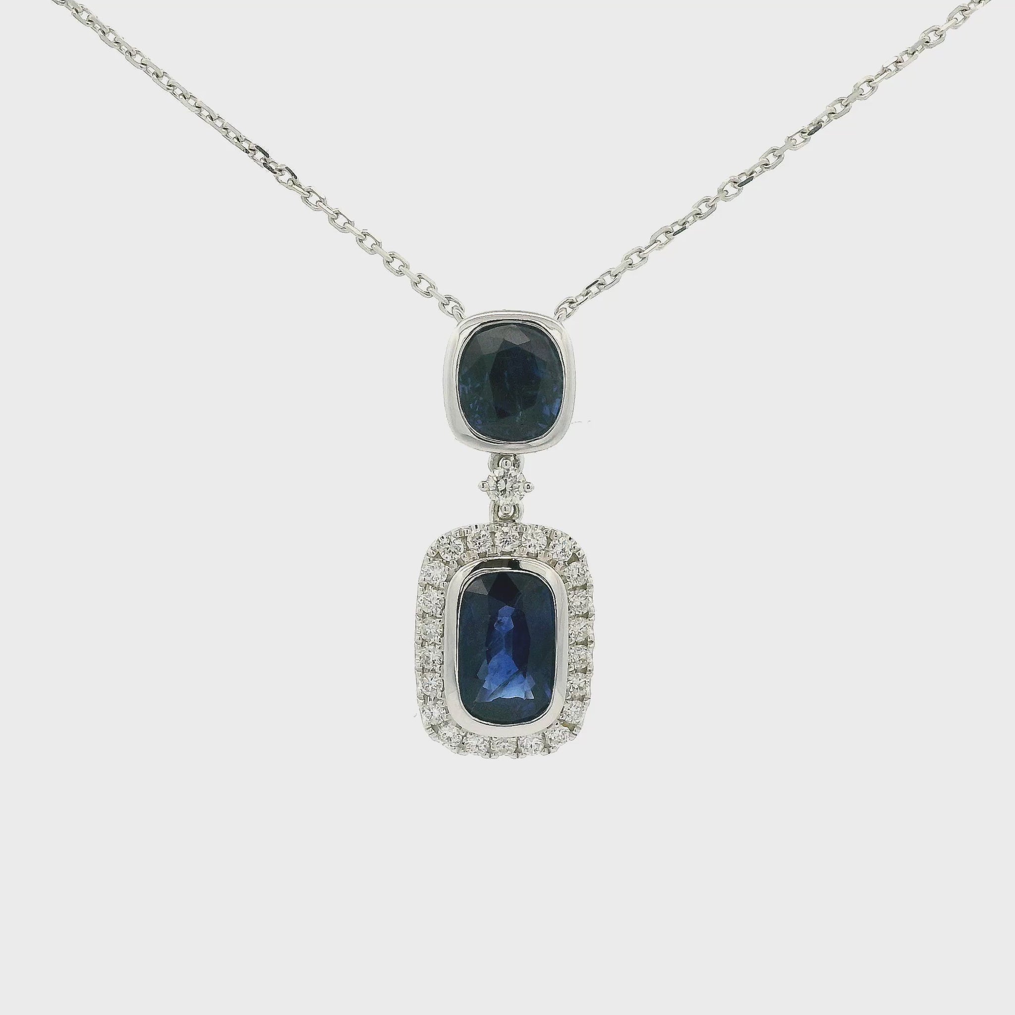 A White Gold Pendant Necklace with two bezel set oval and round cut blue Sapphires in the center with the bottom one having a diamond halo and attached to a diamond by the yard chain at Forever Rox Fine Jewelry, Lake Tahoes Best Jewelry Store