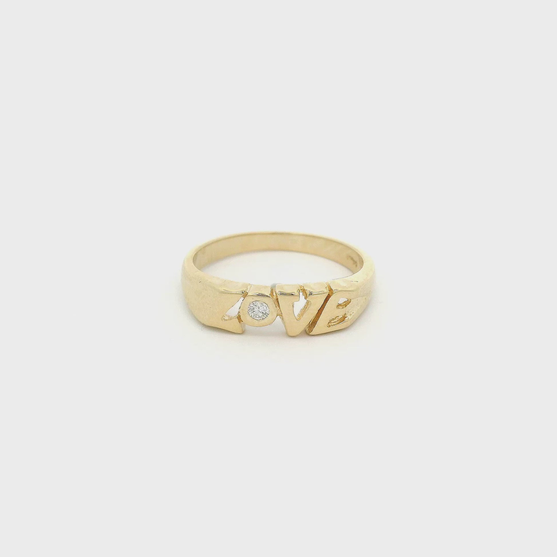 A Yellow Gold Band that says LOVE with a bezel set round cut Dimond in the "o" at Forever Rox Fine Jewelry, Lake Tahoes Best Jewelry Store