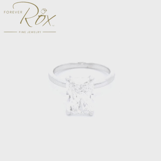 This custom ring features a striking long radiant-cut D color, VS1 clarity diamond, set in sleek 14k white gold. A delicate halo of diamonds surrounds the head below the center stone, creating a clean, modern statement with timeless appeal mad  at Forever Rox Fine Jewelry, Lake Tahoes Best Jewelry Store