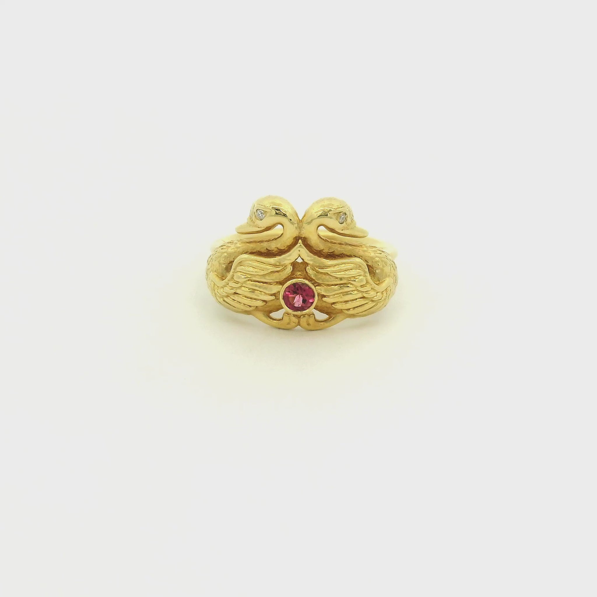 A Yellow Gold Ring with two gold swans and a bezel set round cut natural Electric Pink Tourmaline in the center with diamonds for swan eyes at Forever Rox Fine Jewelry, Lake Tahoes Best Jewelry Store
