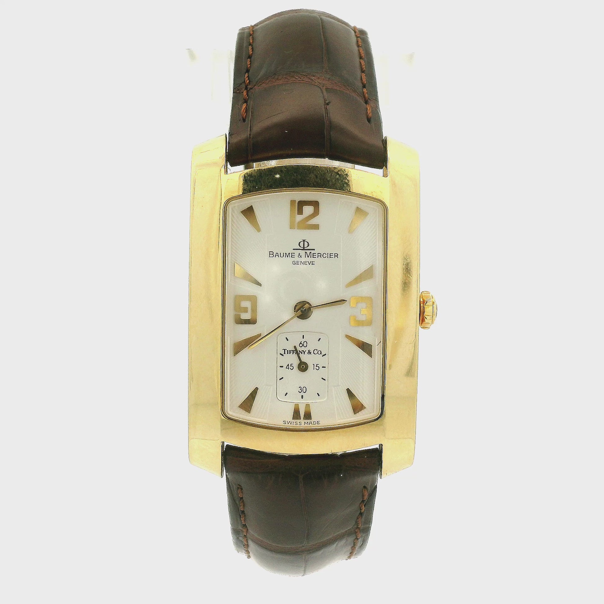 A Vintage Baume & Mercier watch with a 18k gold rectangular case, cream dial with 9, 12 & 3 displayed, the dial is stamped with a tiffany & Co., and dark brown leather strap, shown against a plain white background at Forever Rox Fine Jewelry, Lake Tahoes Best Jewelry Store